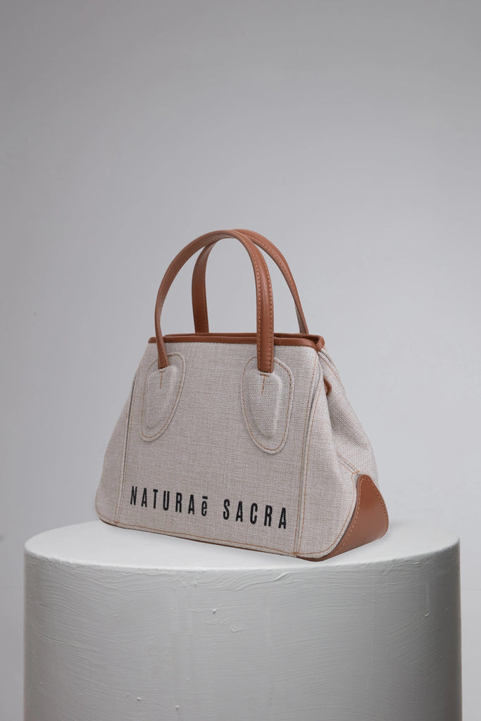 Canvas woman handbag with brand logo front on grey cylinder stand