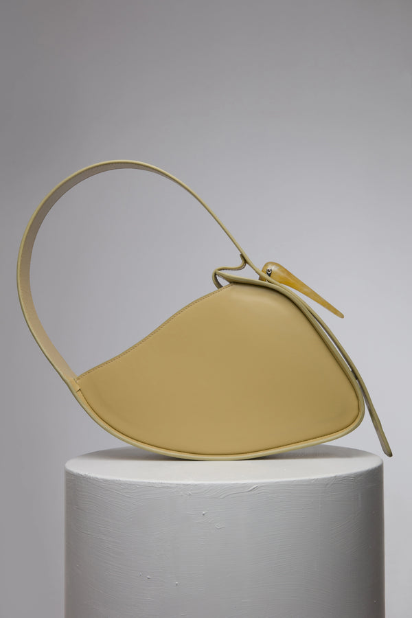 Flat topped oval structured saddle bag with bio resin accessories and non-removable but adjustable calf leather strap on a white stand