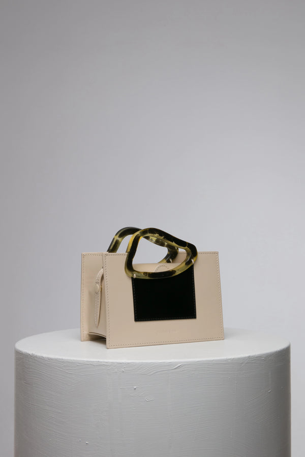 Rectangle shaped beige black colour calf leather saddle bag with natural resin handle holder and remowable calf leather handle strap on a white stand