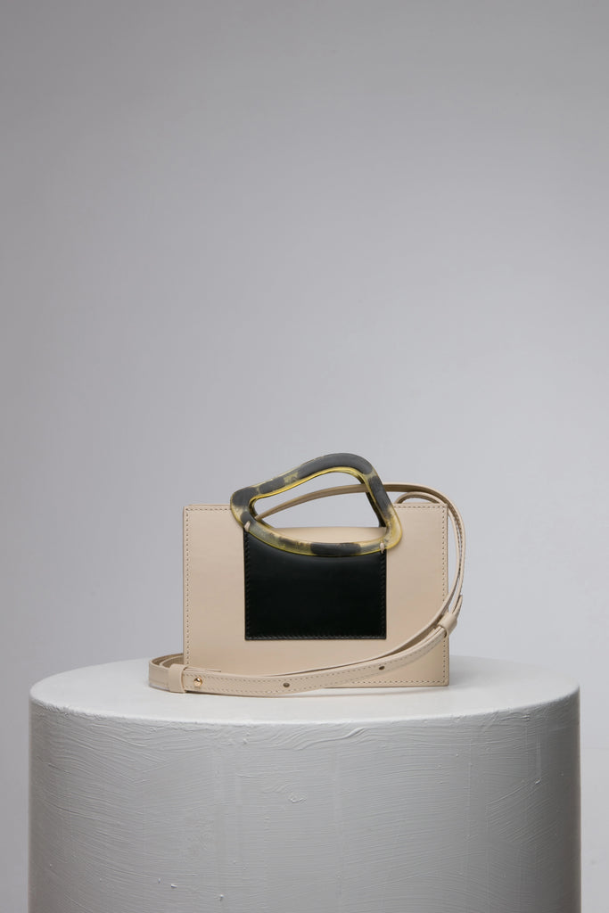 Rectangle shaped beige black colour calf leather saddle bag with natural resin handle holder and remowable calf leather handle strap on a white stand