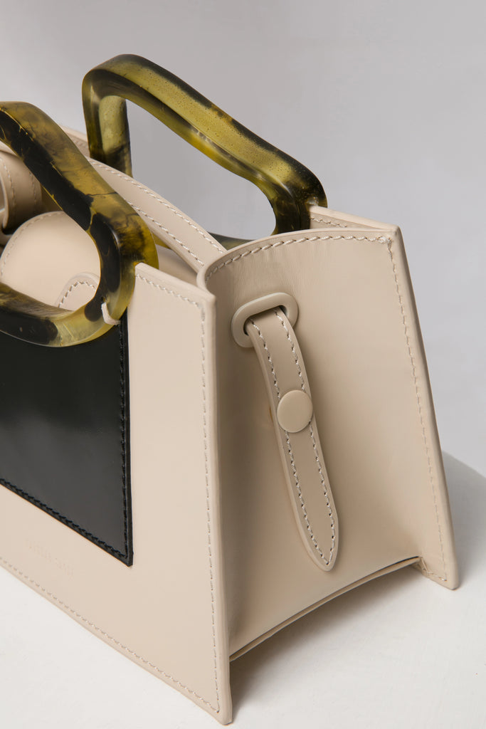 Rectangle shaped beige black colour calf leather saddle bag with natural resin handle holder and remowable calf leather handle strap on a white stand