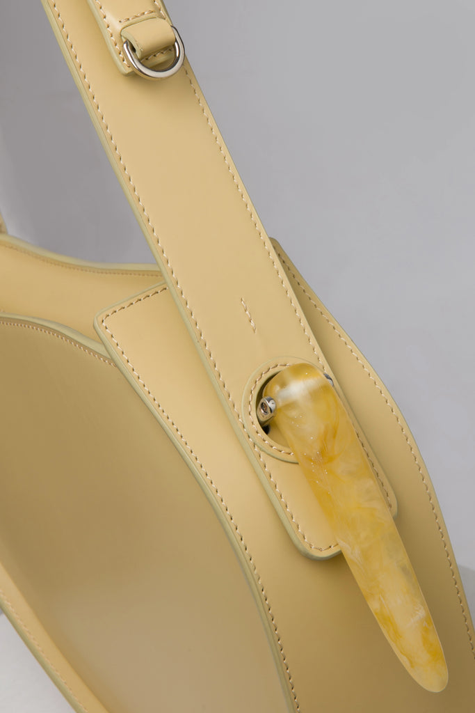 Flat topped oval structured saddle bag with bio resin accessories and non-removable but adjustable calf leather strap on a white stand