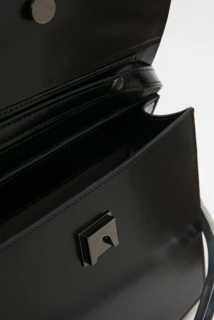 rectangular black leather handbag with metal top handle on white stand