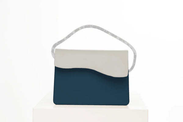 Rectangular women's bag with a blue genuine leather body and bianco flap, bio resin handle and long shoulder handle, on a white stand in the studio