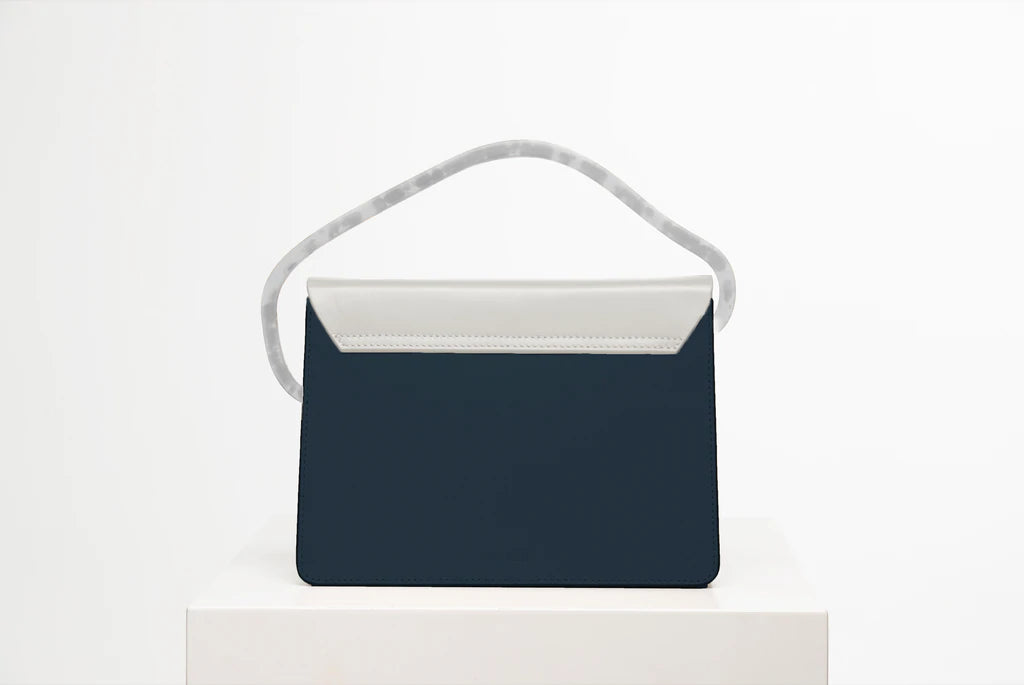 Rectangular women's bag with a blue genuine leather body and bianco flap, bio resin handle and long shoulder handle, on a white stand in the studio