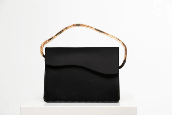 Rectangular women's bag with a black genuine leather body and black flap, bio resin handle and long shoulder handle, on a white stand in the studio
