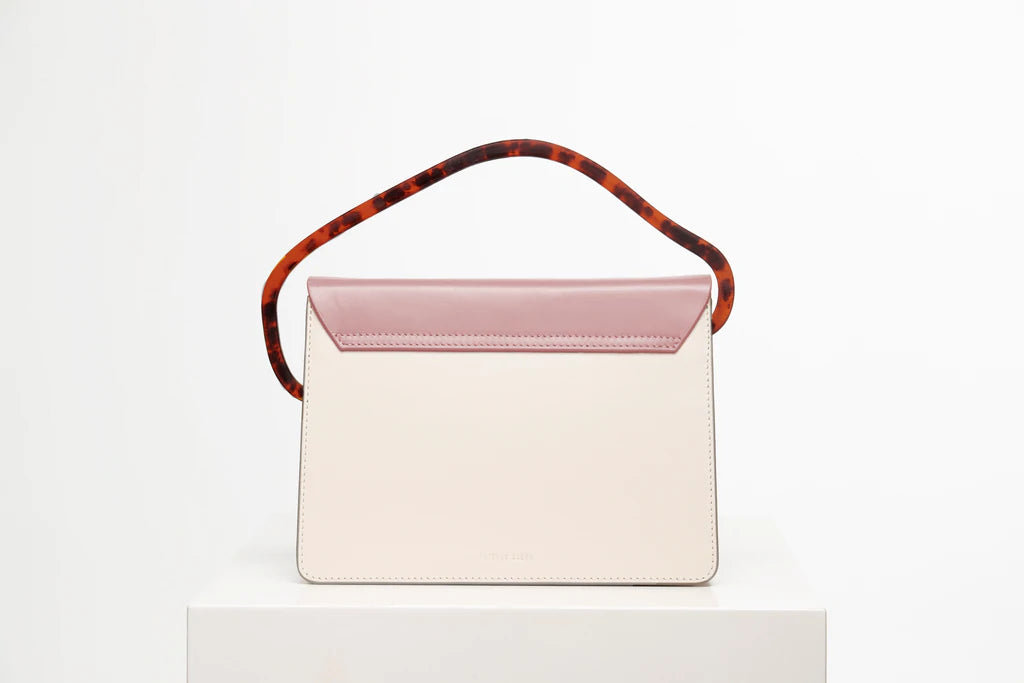 Rectangular women's bag with a bianco genuine leather body and dusty rose flap, bio resin handle and long shoulder handle, on a white stand in the studio