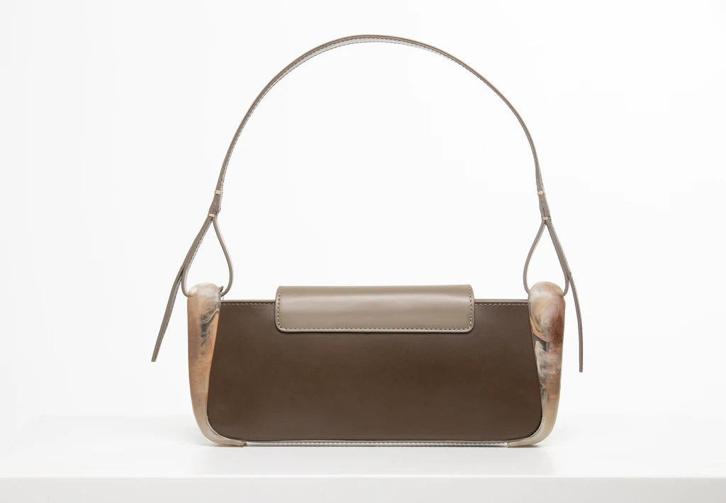 Taupe calf leather rectangle baguette bag with special resin cover companents on the sides. non-removable shoulder strap on a white stand