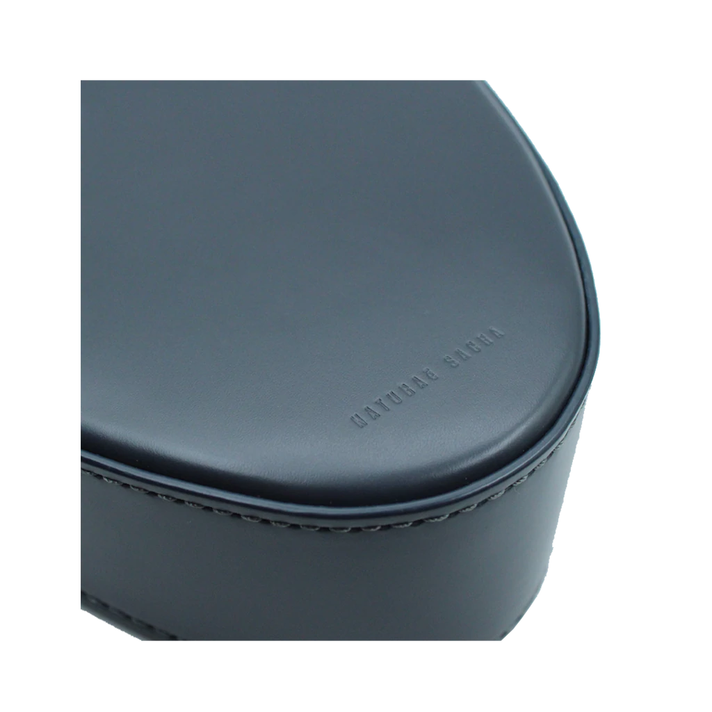 Flap topped oval structured anthracite calf leather cross body bag with an adjustable leather and natural resin chain linked strap on a white stand