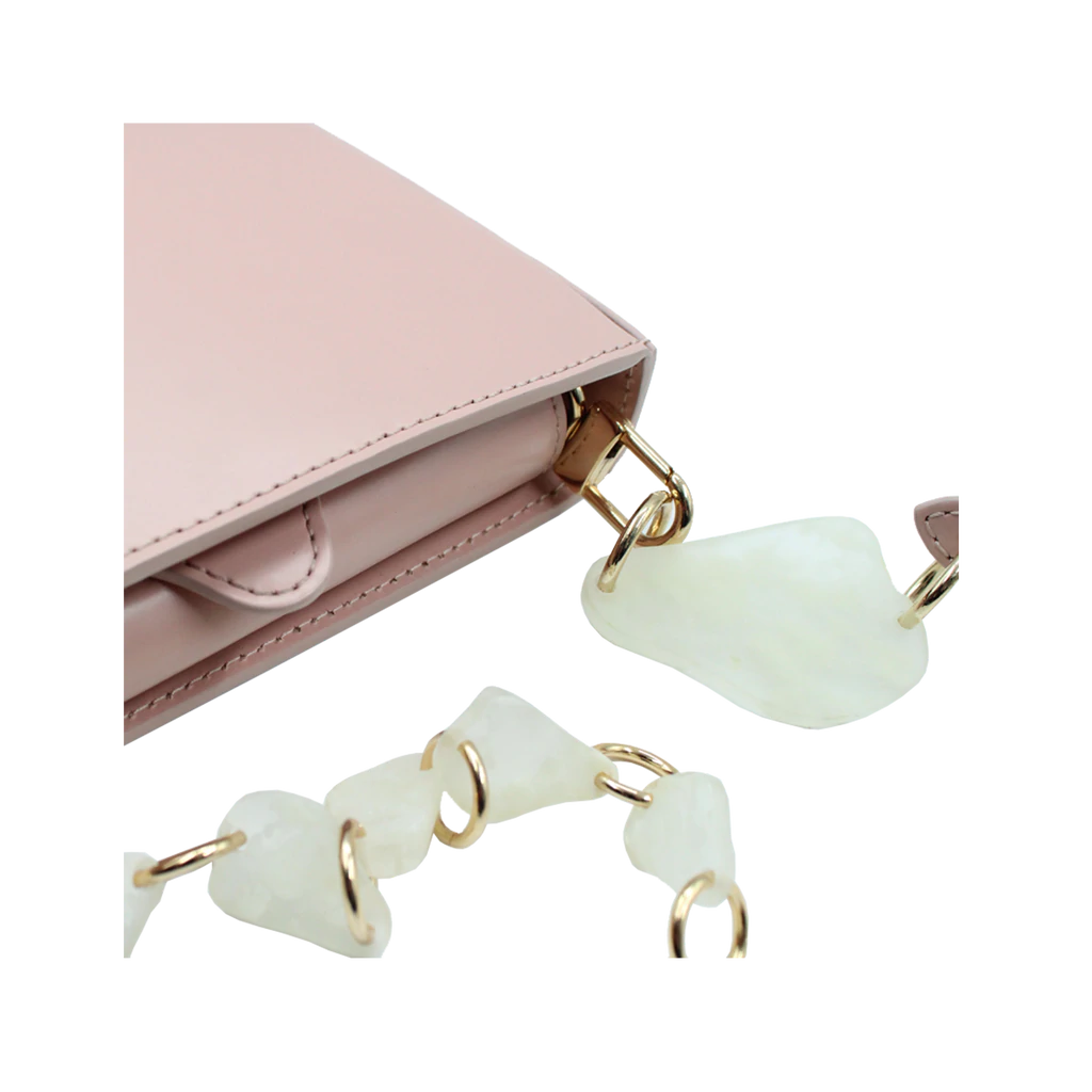 Flap topped oval structured dusty rose calf leather cross body bag with an adjustable leather and natural resin chain linked strap on a white stand