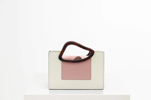 Rectangle shaped dusty rose calf leather saddle bag with natural resin handle holder and remowable calf leather handle strap on a white stand