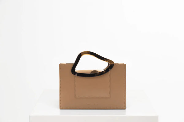 Rectangle shaped champagne calf leather saddle bag with natural resin handle holder and remowable calf leather handle strap on a white stand