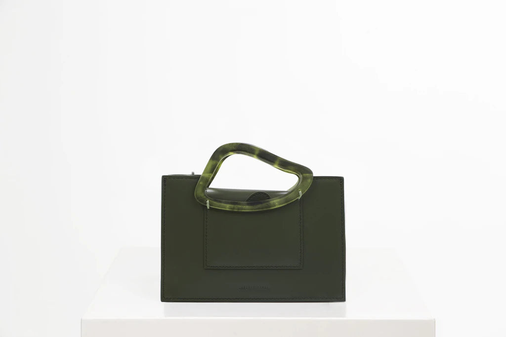 Rectangle shaped olive calf leather saddle bag with natural resin handle holder and remowable calf leather handle strap on a white stand