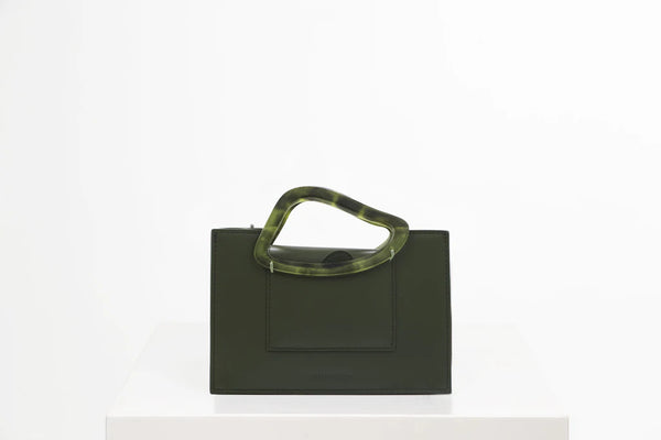 Rectangle shaped olive calf leather saddle bag with natural resin handle holder and remowable calf leather handle strap on a white stand