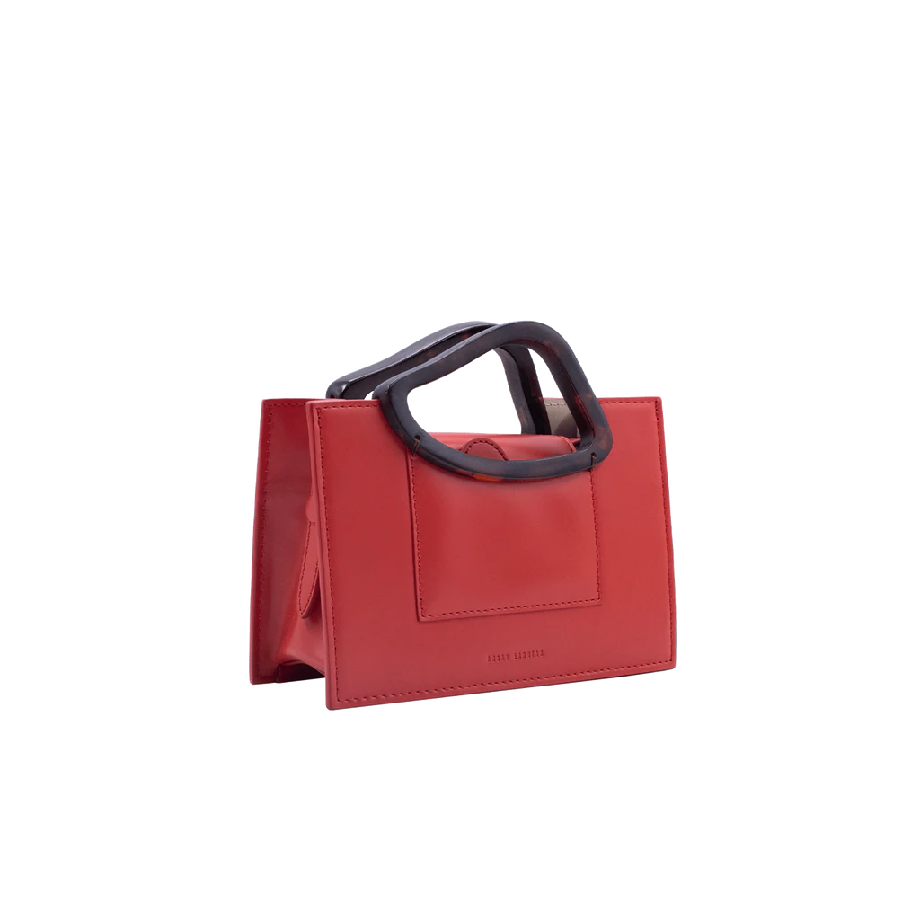 Rectangle shaped red calf leather saddle bag with natural resin handle holder and remowable calf leather handle strap on a white stand