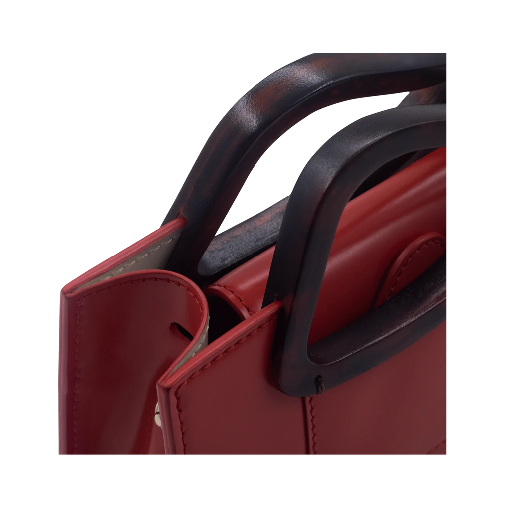 Rectangle shaped red calf leather saddle bag with natural resin handle holder and remowable calf leather handle strap on a white stand