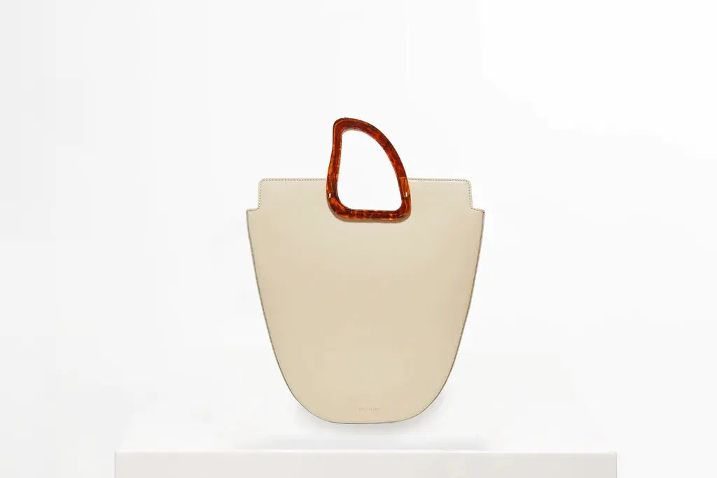 beige leather bag with brown resin handle on white stand