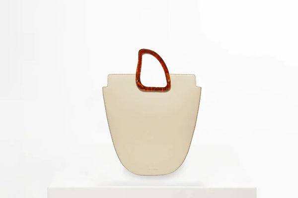 beige leather bag with brown resin handle on white stand