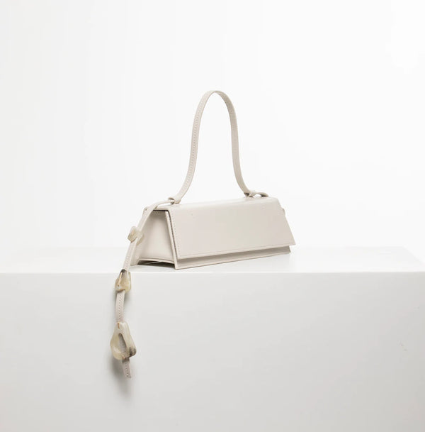 Rectangle shaped off white calf leather clutch bag with natural resin filled in handles and removable calf leather handle strap on a white stand