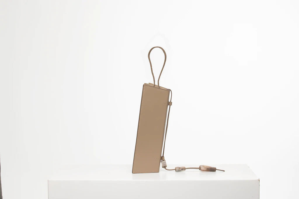 Rectangle shaped taupe calf leather clutch bag with natural resin filled in handles and removable calf leather handle strap on a white stand